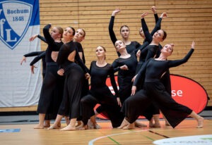 a group of women in black dresses dancing on a basketball court